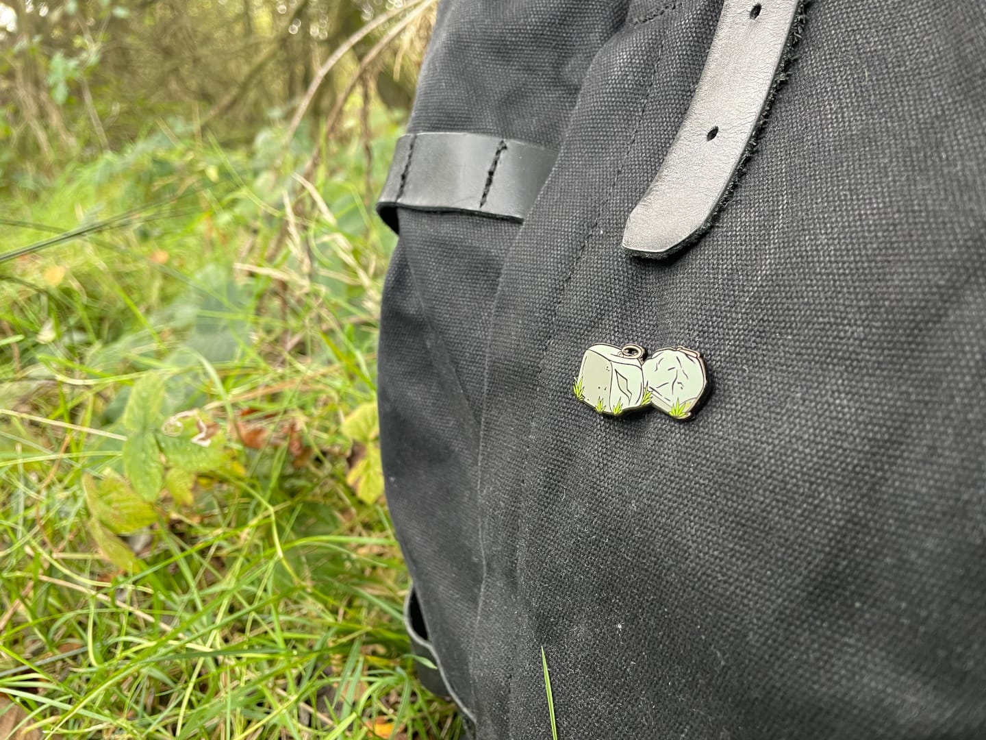 A Dinnie Stones enamel pin on a black backpack outdoors.