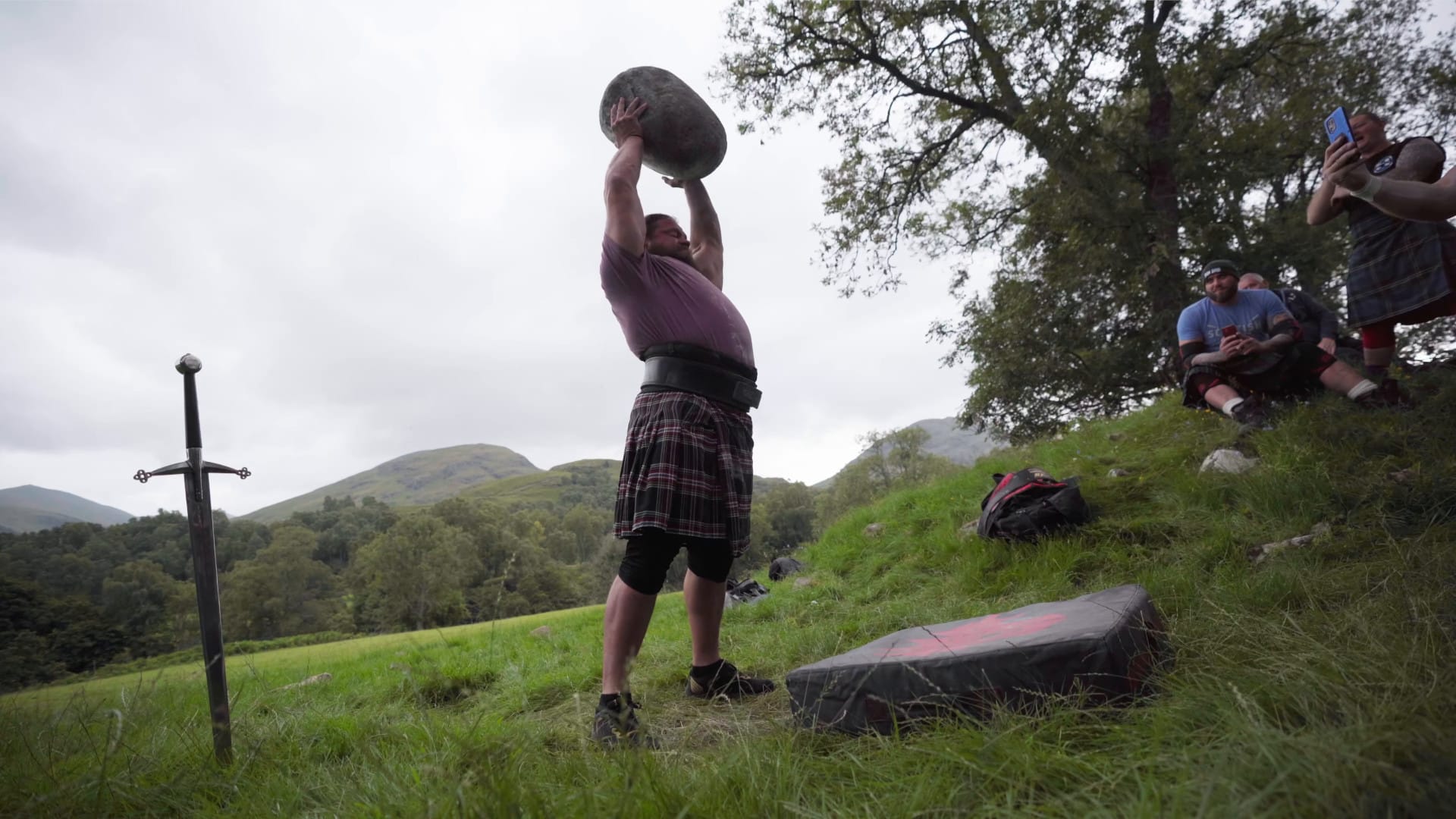 A strongman holds the lifting stone of the Fianna above his head.