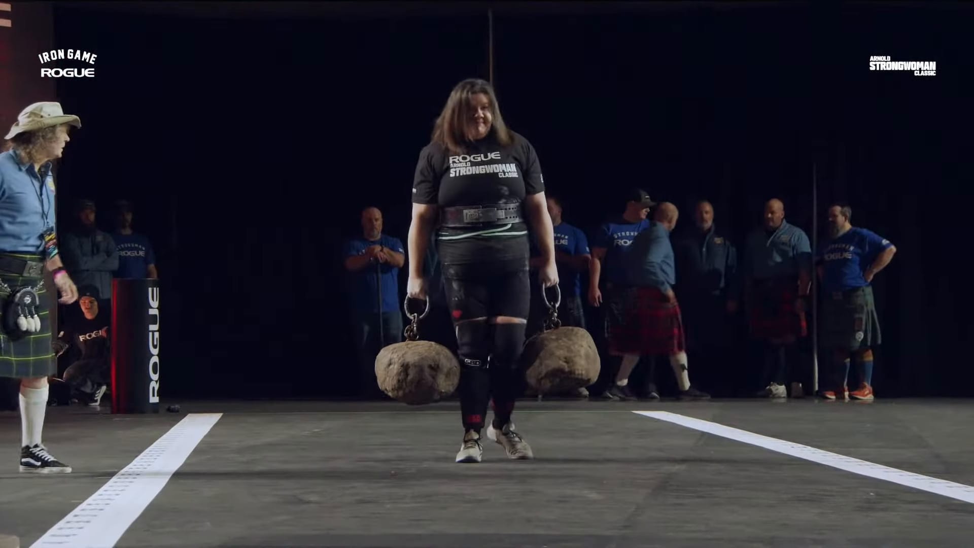 A screenshot from the Arnold Strongwoman Classic livestream. Rebecca Roberts walks with the Jeck Stones down the course. 
