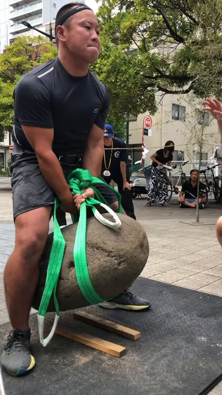 Sakamoto-san holds the Yokozuna stone in the air with a harness wrapped around the stone.