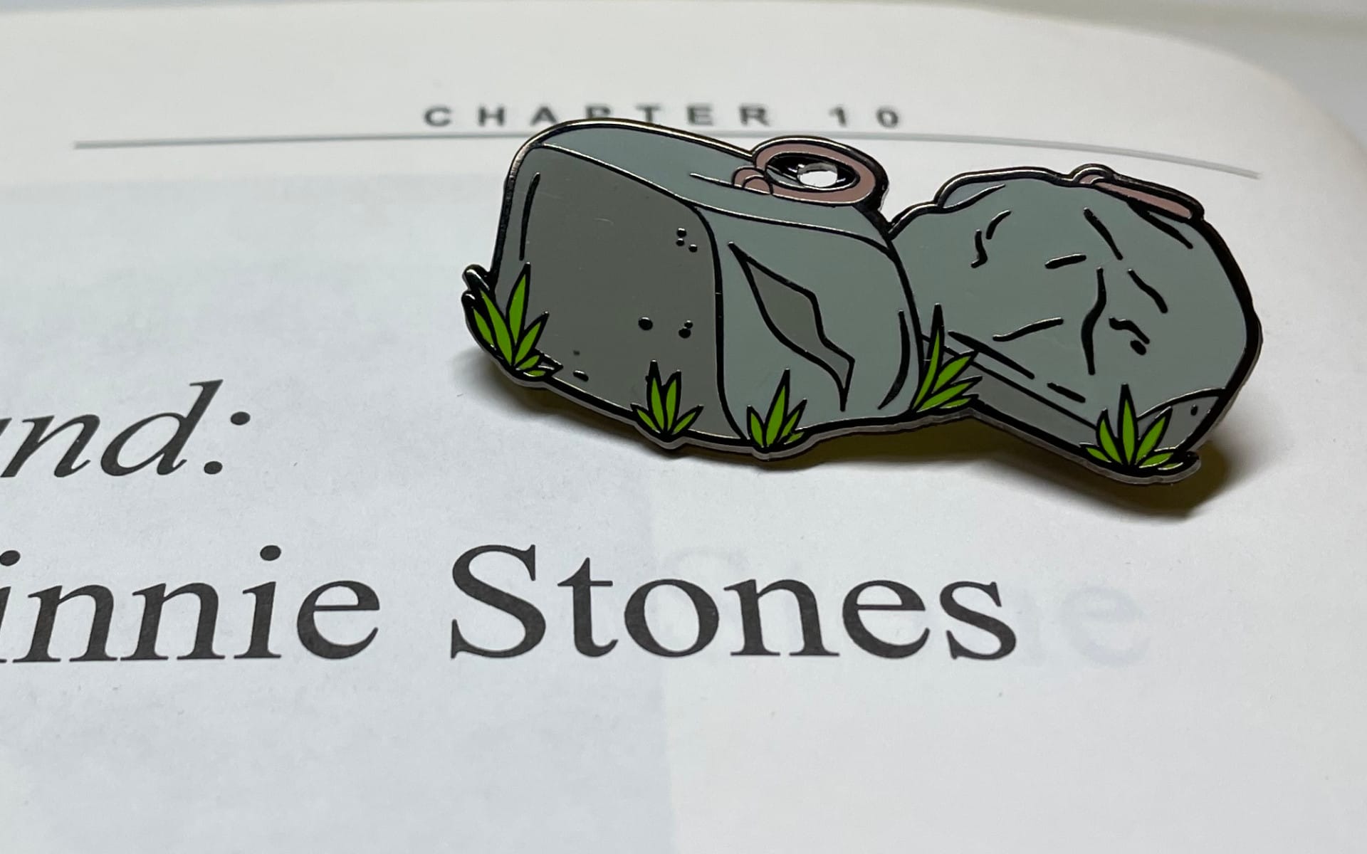 A Dinnie Stones enamel pin sits on a the Dinnie Stones page of 'Of Stones and Strength'.