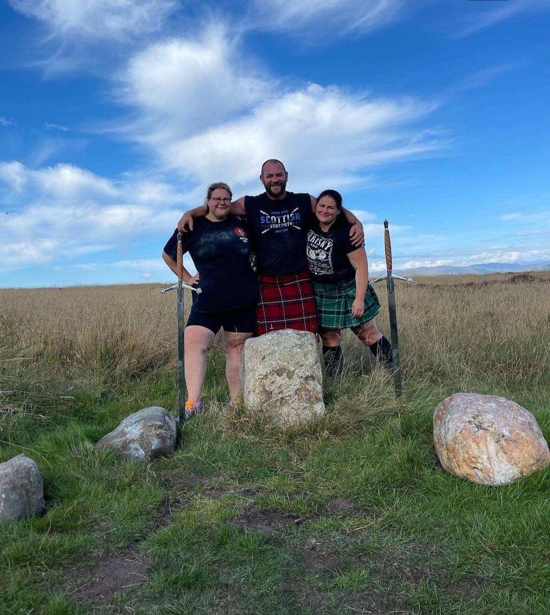 A man stands with two women. They are surrounded by some stones in Sherriffmuir.