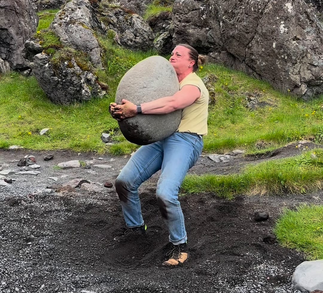 A woman lifts the Fullsturker stone on Djúpalónssandur beach in Iceland.