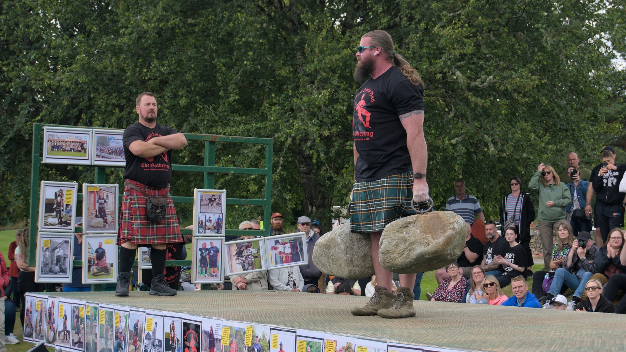 A man with long hair and a beard stands tall with the Dinnie Stones in hand side-by-side.