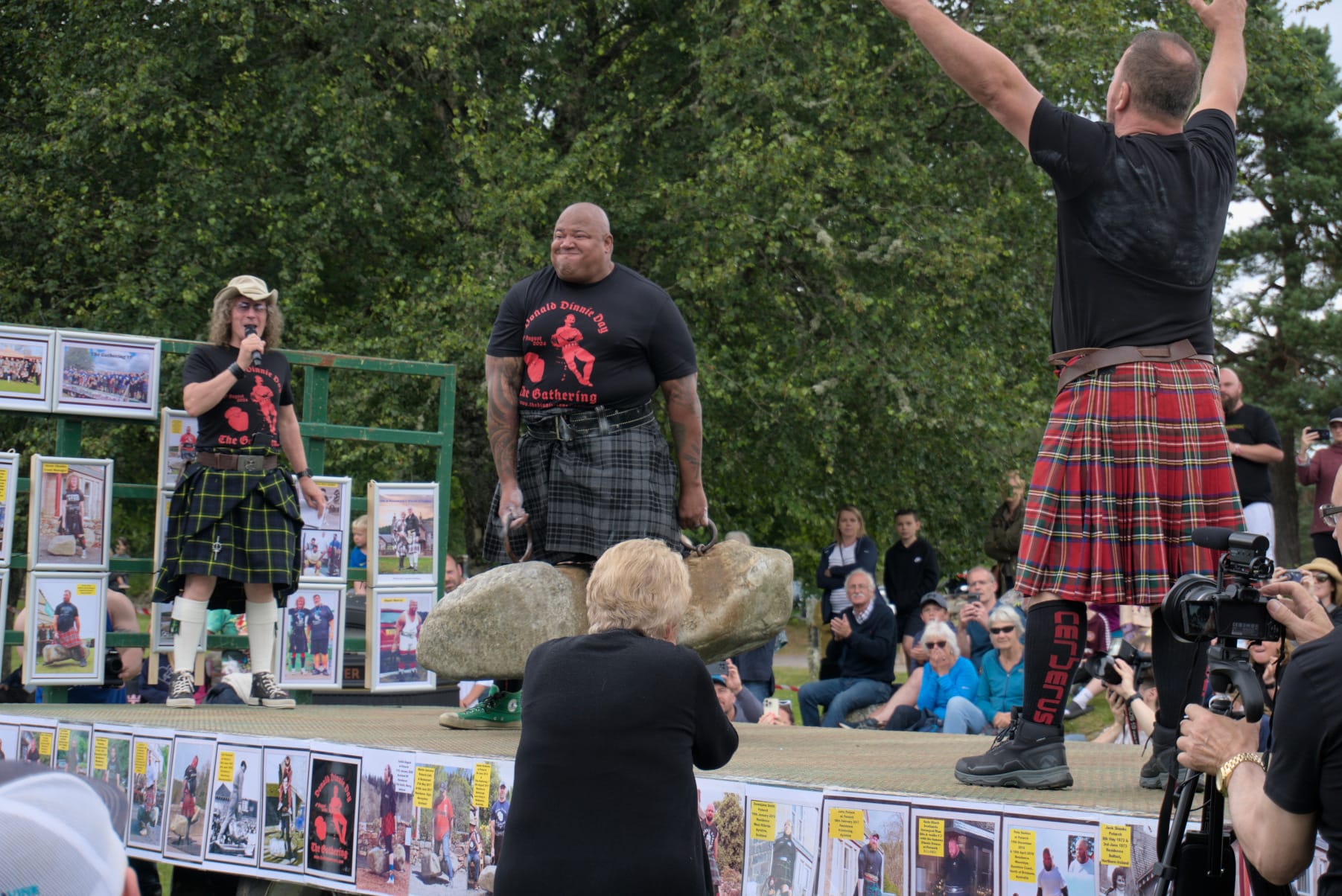 A man with a grimaced face holds the Dinnie Stones in the air. 