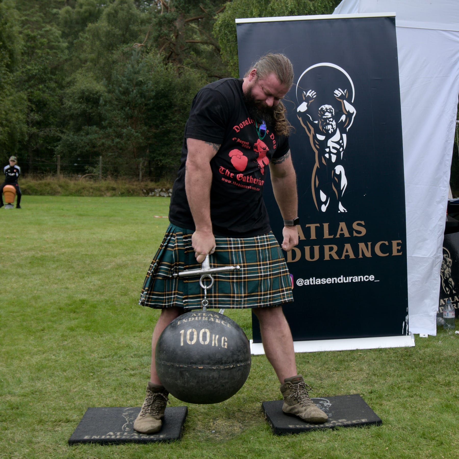 A man lifts a 100kg Atlas Stone in one hand using the hilt of a sword attached via an eyelet on the stone..