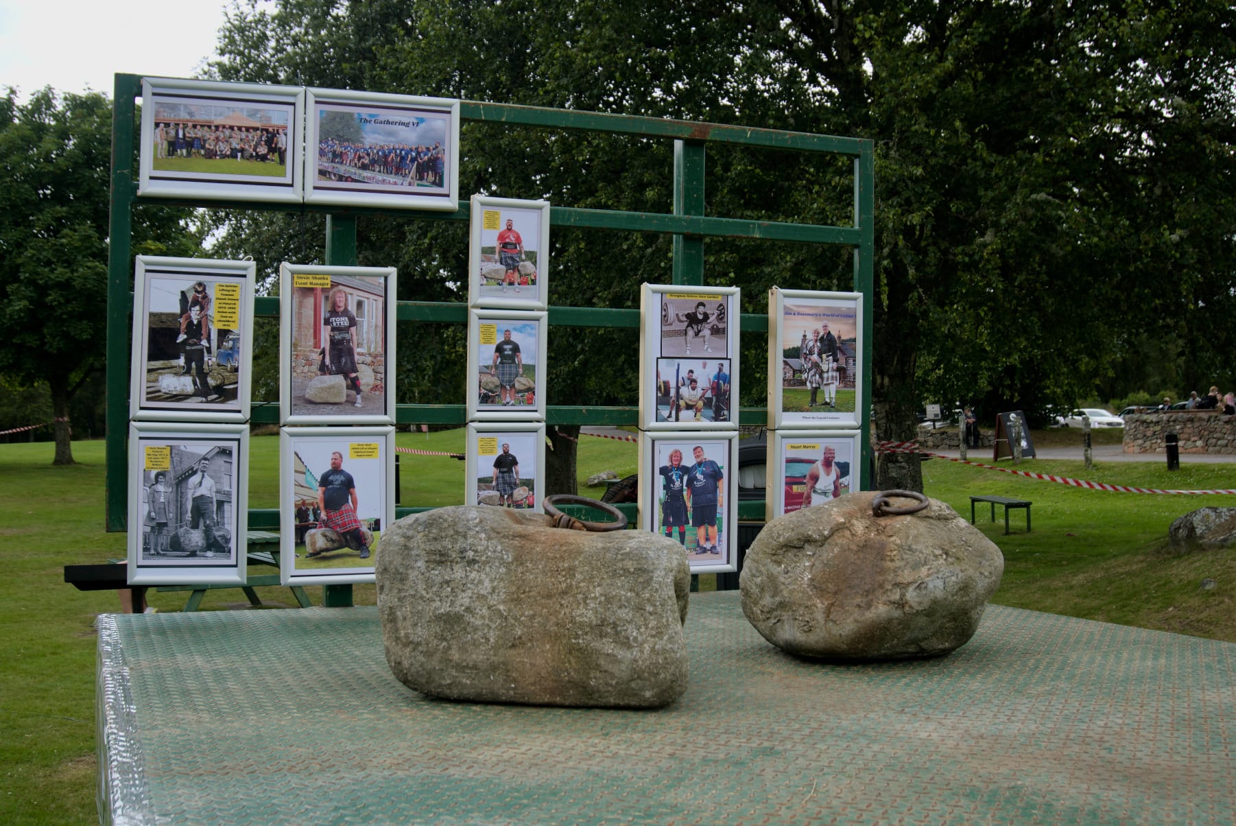 The Dinnie Stones sit on a green metal flatbed. Multiple photos of past lifters hang on the upright at the end of the platform.