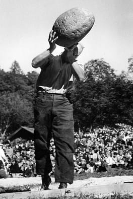 A black and white photo of a man throwing the Unspunnen stone from his shoulder.