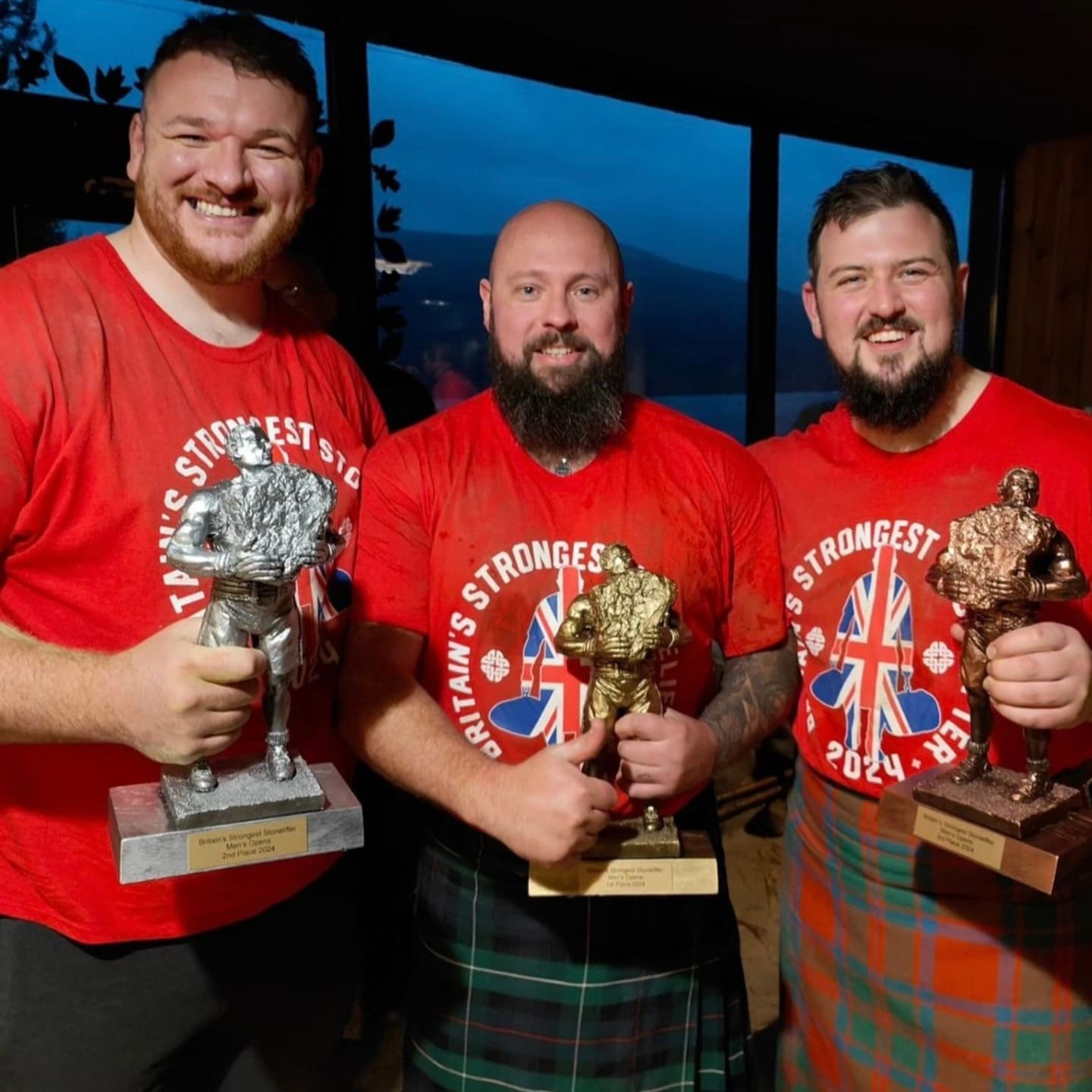 Three men in red competition T-Shirts pose for a photo with their podium trophies.