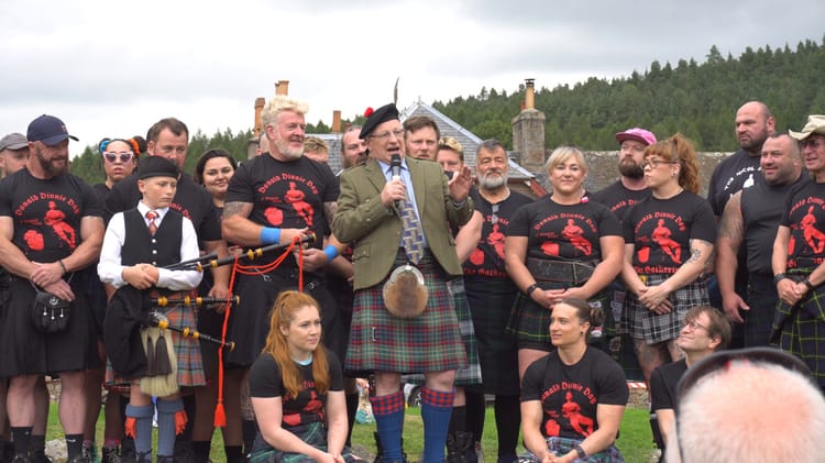 Malcolm Nicol speaks into a microphone with a large group of athletes around him.